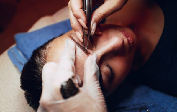 Close up of a beautician hands shaping eyebrows with tweezers to model.