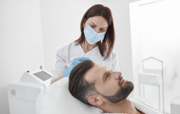 Careful woman beautician with protective mask does medicine injection to man patient during antiaging meso therapy procedure in professional cosmetology clinic